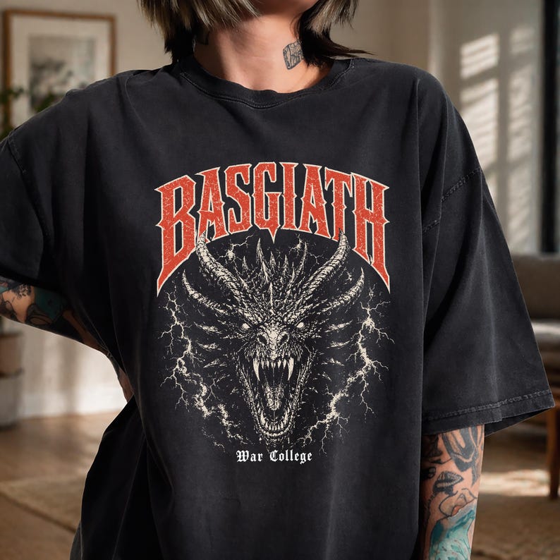 Puede incluir: Camiseta negra con un dise&ntilde;o de drag&oacute;n detallado y la palabra "BASGIATH" en rojo. El texto "War College" est&aacute; debajo. El dise&ntilde;o tiene un aspecto vintage y desgastado, con una ilustraci&oacute;n de drag&oacute;n.