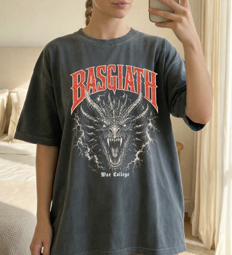 Puede incluir: Camiseta gris oscuro con aspecto desgastado. La parte delantera presenta un gr&aacute;fico rojo y blanco de una cabeza de drag&oacute;n con la palabra "BASGIATH" arriba y "War College" abajo. La camiseta tiene mangas cortas y cuello redondo.