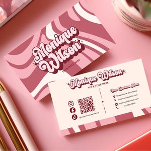 May include: Two business cards with a retro design featuring the name "Monique Wilson" in a swirling font. The cards are in shades of pink and burgundy, with contact information and social media icons.
