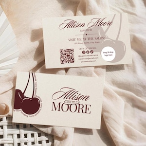 May include: Two rectangular business cards in a cream color with dark red text and cherry graphics. The cards feature the name Allison Moore, the title Lash Tech, a QR code, social media icons, and a placeholder circle for a logo.