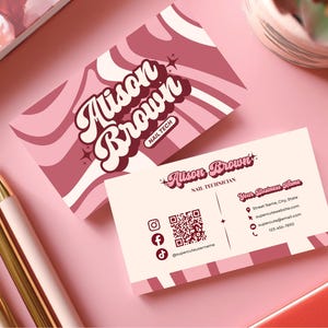 May include: Two business cards with the text "Alison Brown Nail Tech" in a retro font, with a pink and white swirl design. The second card has contact information, including a QR code and social media icons. Gold and pink pens are in the foreground.