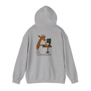 May include: A light gray hoodie featuring a cartoon giraffe working on a computer with the word "DEBUGGING" below. The giraffe is brown with a long neck, and the computer screen displays code. The hoodie has a hood and a kangaroo pocket.