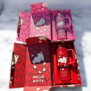 Puede incluir: Dos vasos aislados con tem&aacute;tica de Hello Kitty en sus cajas originales. Uno es rosa, el otro rojo. Ambos presentan el personaje de Hello Kitty y patrones de corazones. Las cajas tambi&eacute;n est&aacute;n decoradas con Hello Kitty y dise&ntilde;os de corazones.