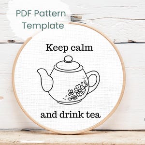 Könnte beinhalten: Ein Stickrahmen mit weißem Stoff. Er zeigt eine schwarze Strichzeichnung einer Teekanne mit floralen Details und dem Text "Keep calm and drink tea". Die Worte "PDF Pattern Template" stehen oben auf dem Rahmen.