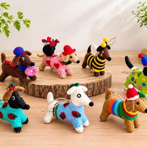 May include: Seven needle-felted dog ornaments in various colours and outfits. One wears a blue hat and holds a pink doughnut, another a red hat with flowers, one is a bee, one has a green polka-dot jumper, two wear ladybird jumpers, and one a rainbow jumper.