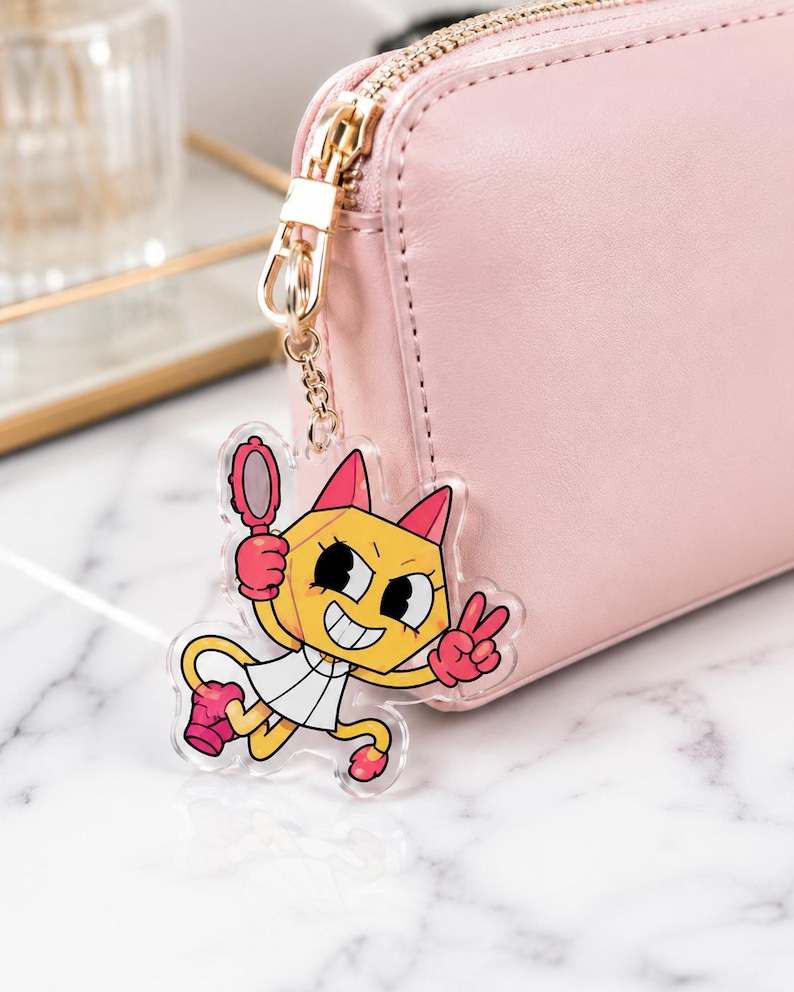 May include: A clear acrylic keychain featuring a cartoon yellow cat character with pink ears, wearing a white dress and pink gloves, holding a small pink hand mirror and making a peace sign, attached to a light pink rectangular zippered wallet.