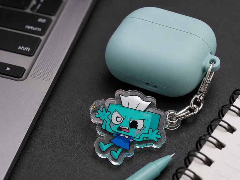 May include: A light blue silicone case for wireless earbuds attached to a clear acrylic keychain charm. The charm features a cartoon character shaped like a teal tissue box with a white tissue on top, wearing a blue dress, with an angry facial expression.