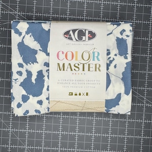 May include: A folded fabric bundle featuring a panda bear pattern in white and blue. The fabric is labeled "COLOR MASTER" by Art Gallery Fabrics. The package includes a beige burlap ribbon and is made of 100% premium cotton.