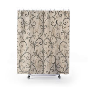 May include: A shower curtain featuring a beige background with a distressed, weathered texture and a repeating dark gray damask pattern of scrolling vines and leaves. The curtain is suspended from a series of silver-toned metal rings at the top.