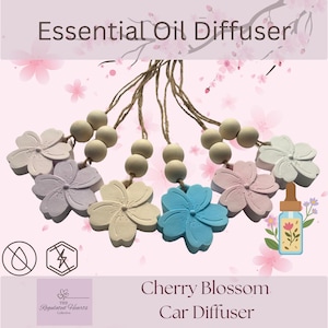 May include: Five hanging essential oil diffusers shaped like cherry blossoms in light purple, cream, blue, and pink. Each features two round wooden beads on a jute twine string. The text reads Essential Oil Diffuser and Cherry Blossom Car Diffuser.