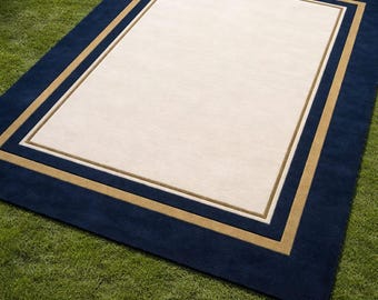 Handgetuft wollen vloerkleed – marineblauwe rand, beige midden, gouden lijnen, minimalistisch tapijt