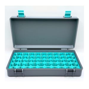 May include: A rectangular gray storage case with a hinged lid and two bright teal latches. The interior features a bright teal foam insert with forty-eight circular cutouts arranged in a grid pattern for organizing small cylindrical items.