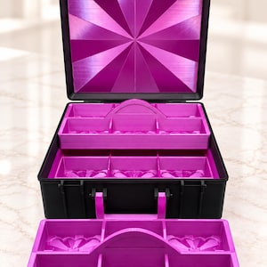 May include: A black storage case with a bright pink interior featuring multiple compartments. The lid has a sunburst pattern, and a removable pink tray with six sections sits in front of the open case, which also contains a tiered tray system.