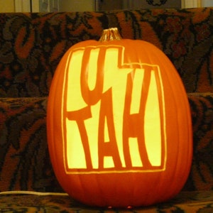 May include: A carved pumpkin with the word "UTAH" illuminated from inside. The pumpkin is orange and the letters are white.