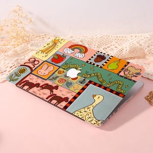 May include: A laptop skin featuring a colorful grid of illustrations including a yellow duck, green caterpillars, a red apple, a rainbow, a brown acorn, a pear, a rabbit face, and brown horses, with a central cutout for the Apple logo.