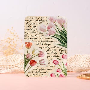May include: A rectangular plaque featuring a vintage-style beige background with black cursive French handwriting. The surface is decorated with illustrations of pink, red, and white tulips with green stems and leaves arranged across the design.