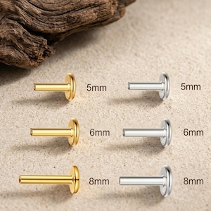 May include: A collection of six flat-back labret studs arranged in two columns. The left column features gold-tone studs in 5mm, 6mm, and 8mm lengths. The right column features silver-tone studs in 5mm, 6mm, and 8mm lengths, with each size clearly labeled.