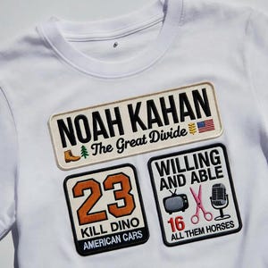 Può includere: T-shirt bianca con tre toppe ricamate. La toppa superiore recita "NOAH KAHAN" e "The Great Divide". La seconda toppa ha il numero "23" e "KILL DINO AMERICAN CARS". La terza toppa dice "WILLING AND ABLE" e "ALL THEM HORSES".