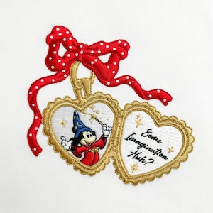 Könnte beinhalten: Gesticktes Design mit einem herzförmigen Medaillon mit Mickey Mouse als Zauberer, der einen Zauberstab hält. Das Medaillon ist goldfarben mit dem Text "Some Imagination Huh?" und wird von einer roten Schleife mit weißen Punkten gekrönt. Das Design befindet sich auf weißem Hintergrund.