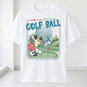 Op de afbeelding: Wit T-shirt met een cartoonafbeelding van Mickey Mouse die golf speelt. Het ontwerp bevat de tekst "I thought it was a GOLF BALL" in een blauw en rood kader, met een golfbaan en een grote bol op de achtergrond.