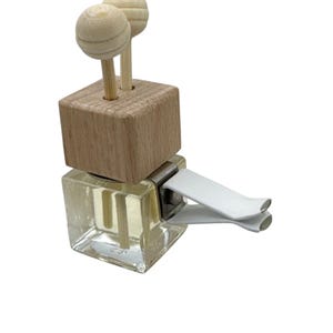 May include: A square glass car air freshener bottle filled with clear liquid, topped with a light-colored wooden block and two small wooden spheres on sticks. A white plastic clip is attached to the side for mounting onto a vehicle vent.