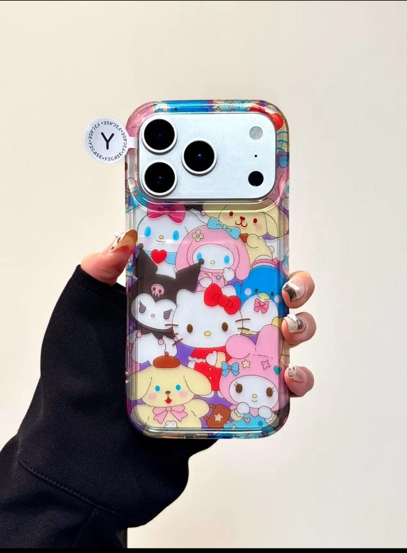 May include: Clear phone case featuring a colorful collage of cartoon characters, including Hello Kitty and friends. The case has a transparent border and a multi-colored design on the top. A small, circular sticker with the letter "Y" is visible.