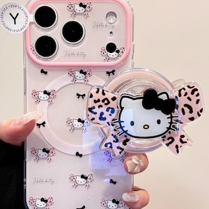 A clear Hello Kitty phone case with a pink bumper is shown held in hand with a large Hello Kitty-shaped grip attached to the back.