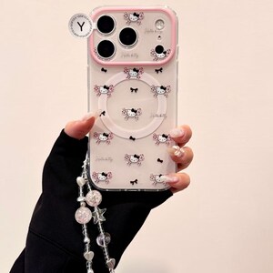 A clear Hello Kitty phone case with a pink bumper is shown front-on with a large Hello Kitty grip and a dangling beaded wristlet.