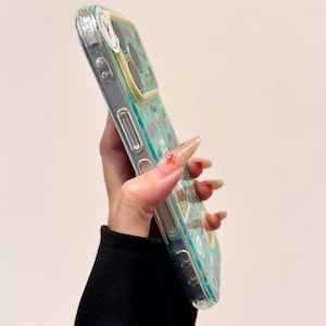 Puede incluir: Funda de tel&eacute;fono transparente con un dise&ntilde;o colorido con personajes de dibujos animados y elementos florales. La funda tiene un fondo azul claro y un &aacute;rea de c&aacute;mara amarilla. La funda est&aacute; hecha de un material transparente.