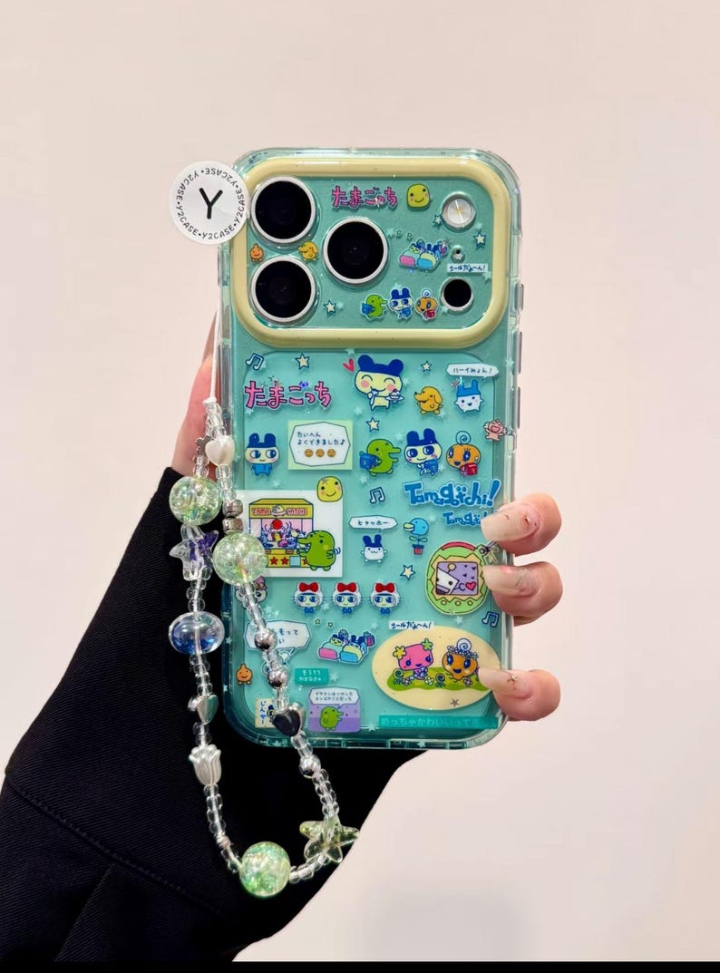 Puede incluir: Una funda transparente para tel&eacute;fono con un fondo turquesa y personajes de dibujos animados coloridos. La funda tiene un borde amarillo y una correa de cuentas con cuentas transparentes y verdes. Se ve texto japon&eacute;s.