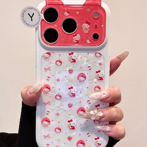 A hand holds a Hello Kitty phone case with a red cat-ear camera section and a pearly white patterned back.