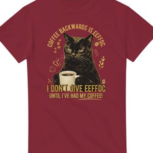 Könnte beinhalten: Ein bordeauxrotes Kurzarm-T-Shirt mit einer Grafik einer schwarzen Katze, die eine weiße Kaffeetasse hält. Der Text lautet: COFFEE BACKWARDS IS EEFFOC. I DON'T GIVE EEFFOC UNTIL I'VE HAD MY COFFEE! Das Design enthält kleine Kaffeebohnen-Symbole.