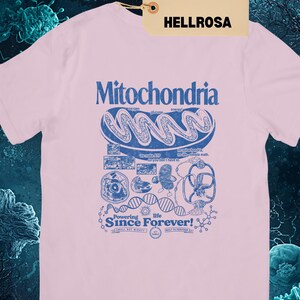 A light pink short-sleeve t-shirt with a blue graphic of a mitochondria cell and related scientific diagrams and text, with a brown tag that says "LIGHT PINK HELLROSA."