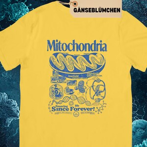 A yellow short-sleeve t-shirt with a blue graphic of a mitochondria cell and related scientific diagrams and text, with a brown tag that says "DAISY GÄNSEBLÜMCHEN."