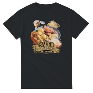 Può includere: Una t-shirt nera a maniche corte con una grafica raffigurante un piatto con patate, salsiccia e crauti, insieme a un hot dog e un barattolo. Sotto il cibo, un nastro dorato mostra il testo: SAUER IS THE NEW SWEET SINCE TRADITION.