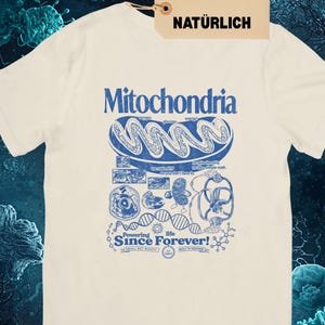 A cream-colored short-sleeve t-shirt with a blue graphic of a mitochondria cell and related scientific diagrams and text, with a brown tag that says "NATURAL NATÜRLICH."