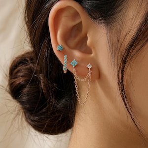 May include: A collection of gold-toned earrings, including a star-shaped stud with turquoise stones, a small hoop with turquoise accents, a flower-shaped stud with turquoise stones, and a chain-linked earring with a clear stone.
