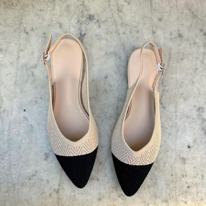 Könnte beinhalten: Ein Paar beige Slingback-Flats mit schwarzen, spitzen Zehen. Die Schuhe haben eine gewebte Textur auf dem Obermaterial und einen Schnallenverschluss am Knöchelriemen. Der Innenraum ist hellbeige.