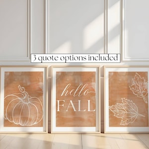 May include: Three framed wall art prints with a burnt orange watercolor background. The left print features a white line drawing of a pumpkin. The center print displays the white text "hello FALL". The right print shows two white line-drawn leaves.