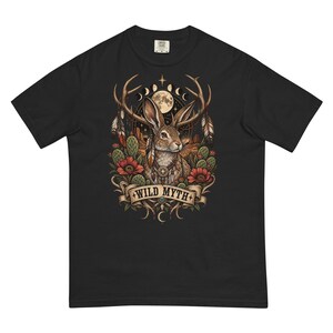 May include: A black short-sleeve t-shirt featuring a graphic print of a jackalope with antlers, feathers, cacti, and red flowers. Above the rabbit is a moon phase cycle and a full moon. A banner at the bottom contains the text WILD MYTH.