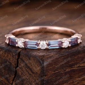 May include: A rose gold ring with alternating rectangular blue-purple gemstones and round white gemstones. The ring is set on a dark wooden surface, with the words "Aurum Ring" repeated around the image.
