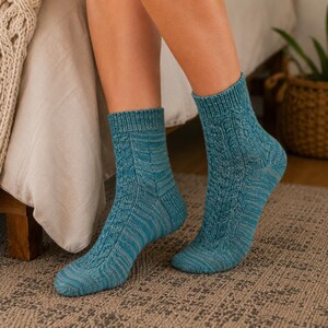 May include: A pair of mid-calf knit socks in a vibrant teal blue color. The socks feature a vertical cable knit pattern running down the front, complemented by a ribbed cuff at the top and a subtle heathered texture throughout the fabric.