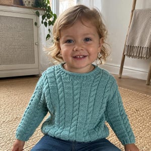 May include: A long-sleeved, teal-colored knitted sweater featuring a vertical cable knit pattern and a ribbed crew neckline. The garment is constructed with a textured stitch design, long sleeves with ribbed cuffs, and a ribbed hem at the waistline.