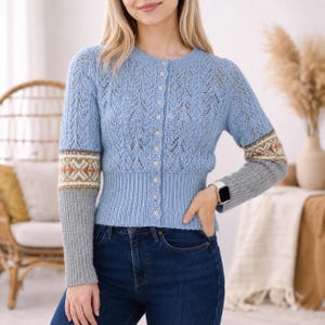 May include: A light blue long-sleeve cardigan with a delicate openwork knit pattern on the bodice. The sleeves feature a horizontal band with a geometric pattern in white, green, and brown, ending in solid grey ribbed cuffs and a button-up front.
