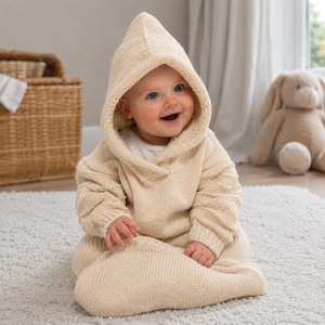 May include: A cream-colored knitted hooded sweater with long sleeves and a textured cable knit pattern on the arms. The garment features a pointed hood and ribbed cuffs, providing a cozy, full-coverage design for a small child to wear comfortably.