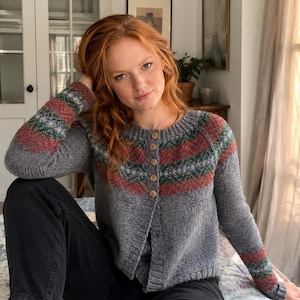 May include: A grey knit cardigan featuring a round neckline and a front button closure with five light brown wooden buttons. The garment displays a horizontal fair isle pattern across the chest and sleeves in shades of red, green, and white.