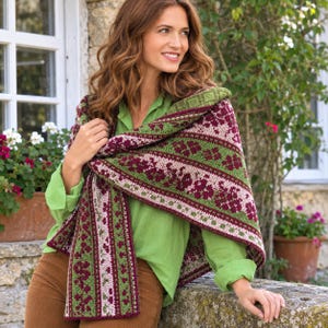 May include: A knitted shawl featuring a repeating floral and geometric pattern in shades of deep burgundy, sage green, and cream. The rectangular accessory is draped over the shoulders, showcasing a dense, textured knit construction with intricate borders.