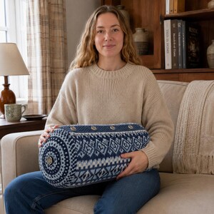 May include: A cylindrical bolster pillow featuring a blue and white knit pattern with geometric motifs. The pillow is accented with a row of four metallic buttons along the top edge and a single matching button centered on the circular side panel.