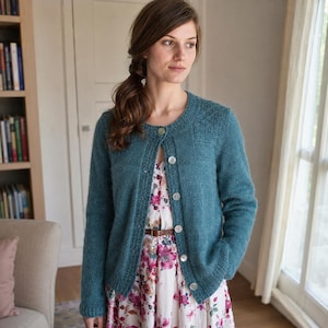 May include: A teal long-sleeved knit cardigan featuring a round neckline, a button-down front with light-coloured buttons, and ribbed cuffs and hem. The cardigan is worn over a white dress with a pink and red floral pattern and a thin brown belt.