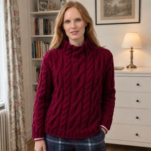 May include: A deep burgundy long-sleeve jumper featuring a prominent vertical cable knit pattern, a high mock neck collar, and ribbed cuffs with thin white stripes at the edges, worn over dark plaid trousers with a visible white grid pattern.